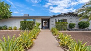 A modern house with a central entrance, surrounded by a pathway and various plants. - Fashion Square Apt3 (Scottsdale)