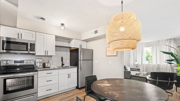 A modern kitchen with stainless steel appliances, a round dining table, and a hanging light fixture. - Fashion Square Apt3 (Scottsdale)