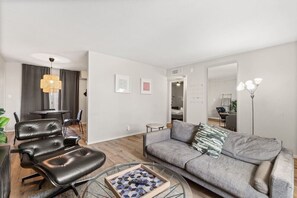 Una sala moderna con un sofá gris, sillas de cuero negro, una mesa de centro de vidrio y una zona de comedor con mesa y sillas.