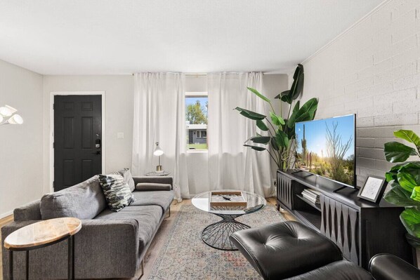 Una sala de estar moderna con un sofá gris, una mesa de centro, un televisor sobre un mueble negro y una planta grande.