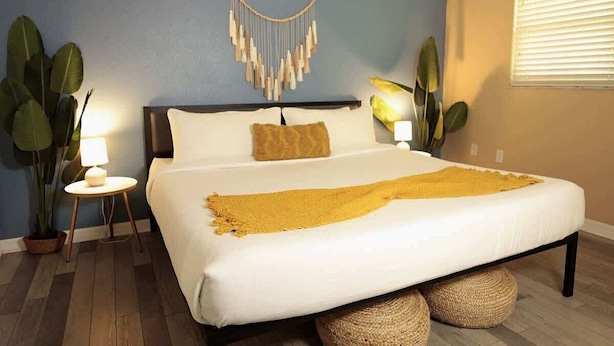 A bedroom with a bed, a wall-mounted macrame piece, two potted plants, and a bedside lamp. - Calm Japandi Retreat With Patio, Near Downtown (Sarasota)