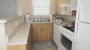 A compact kitchen with wooden cabinets, a white refrigerator, a stove, and a sink. - Calm Japandi Retreat With Patio, Near Downtown (Sarasota)