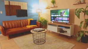 A living room with a brown leather sofa, a round coffee table, a TV on a stand, and a potted plant. - Calm Japandi Retreat With Patio, Near Downtown (Sarasota)