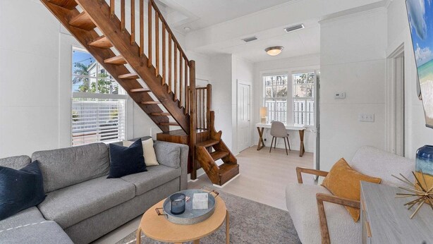A living room with a wooden staircase, a grey sofa, a round coffee table, and a dining area with a white table and chairs. - Tay307-b (Punta Gorda)