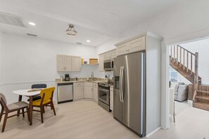 A kitchen with white cabinets, a stainless steel refrigerator, a microwave, and a stove. There is a dining table with chairs. - Tay307-b (Punta Gorda)