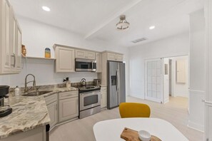 A modern kitchen with white cabinetry, stainless steel appliances, a marble countertop, and a yellow chair. - Tay307-b (Punta Gorda)