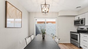 A modern kitchen with a dining area, featuring a large wooden table, white chairs, and a hanging light fixture. - Fashion Square Apt2 Swvillage Scottsdale 8plex (Scottsdale)