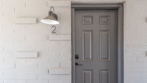 A gray door with a number '2' above it, a doorbell, and a wall-mounted light fixture. - Fashion Square Apt2 Swvillage Scottsdale 8plex (Scottsdale)