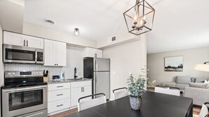 A modern kitchen with white cabinets, a black countertop, stainless steel appliances, and a dining area with a black table and chairs. - Fashion Square Apt2 Swvillage Scottsdale 8plex (Scottsdale)