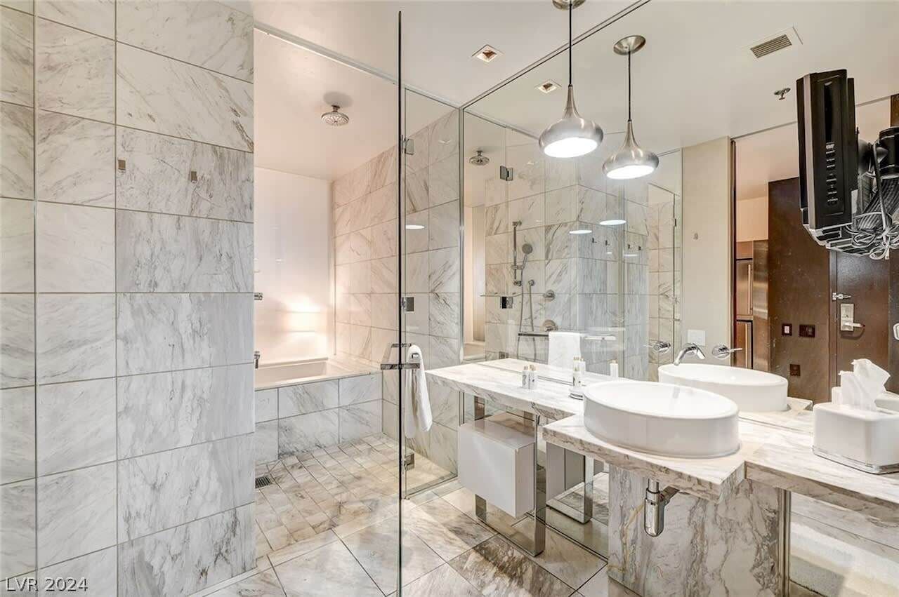 A modern bathroom with marble tiles, a glass-enclosed shower, and a vanity with two sinks.