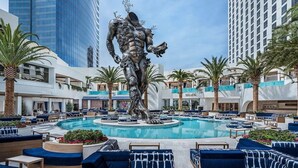 A swimming pool area with a central sculpture, surrounded by lounge seating and palm trees, with high-rise buildings in the background. - Beautiful Mountain-views Studio at the Palms 1107 (Las Vegas)