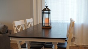 Uma mesa de jantar com cadeiras brancas e um banco, uma vela em um candeeiro e uma janela com cortinas.