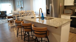 Cozinha com bancada de granito, eletrodomésticos de aço inoxidável e área com banquetas.