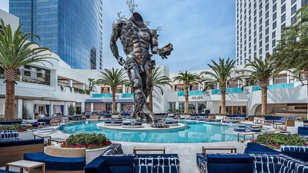 A swimming pool area with a central sculpture, surrounded by lounge seating and palm trees, with high-rise buildings in the background. - Beautiful Strip-view Balcony Access Studio 31318 (Las Vegas)