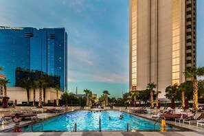 A swimming pool with lounge chairs and palm trees, surrounded by tall buildings. - MGM 10719 Signature Strip View Studio (Las Vegas)