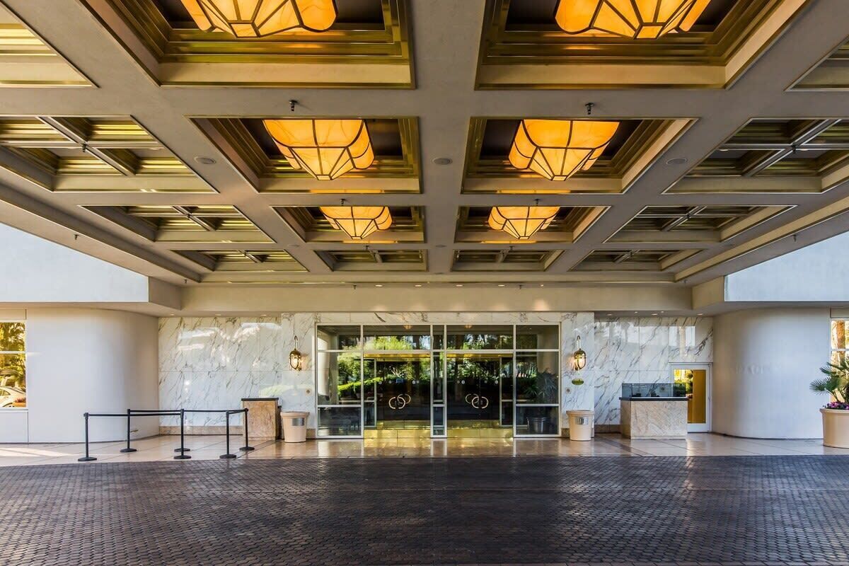 Entrada d'hotel amb un disseny modern, que destaca un taulell de recepció de marbre, portes de vidre i un sostre amb relleus i il·luminació empotrada.
