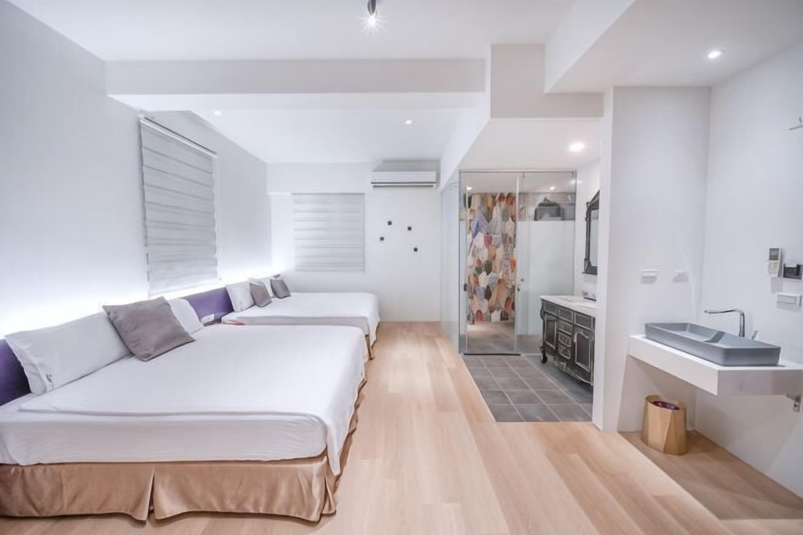 Une chambre d’hôtel moderne équipée de trois lits, d’une kitchenette et d’une salle de bain.