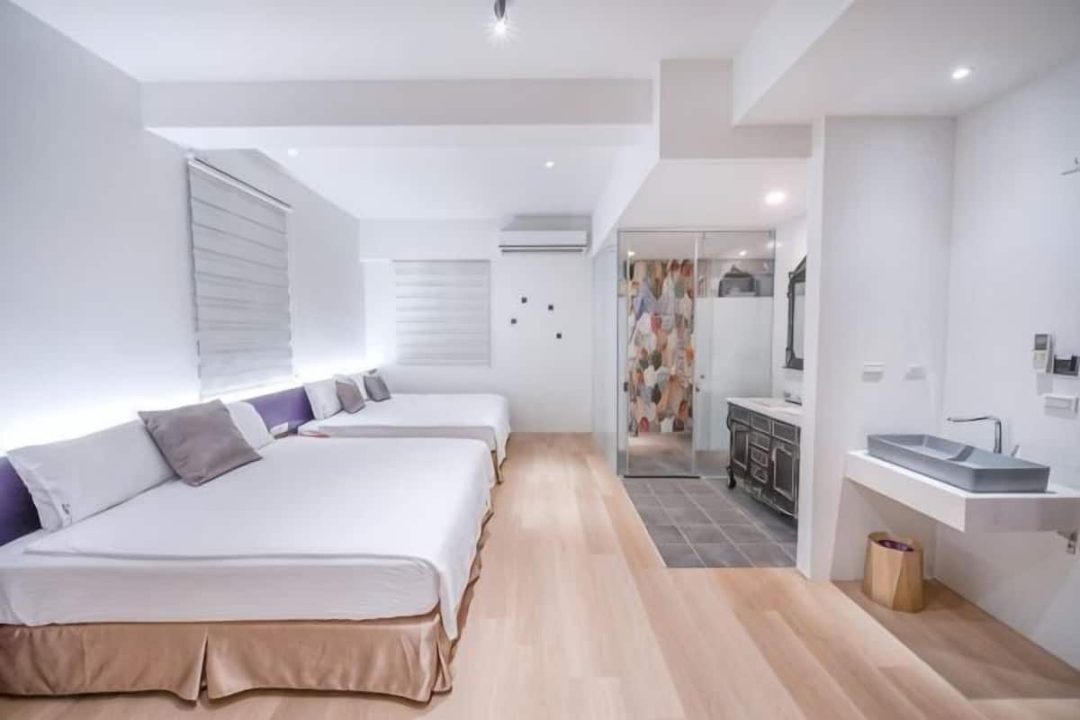 Ein modernes Hotelzimmer mit drei Betten, einer Küchenzeile und einem Badezimmer.