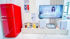 Un salon moderne avec un réfrigérateur rouge, un téléviseur fixé au mur et une étagère où sont exposées diverses figurines.