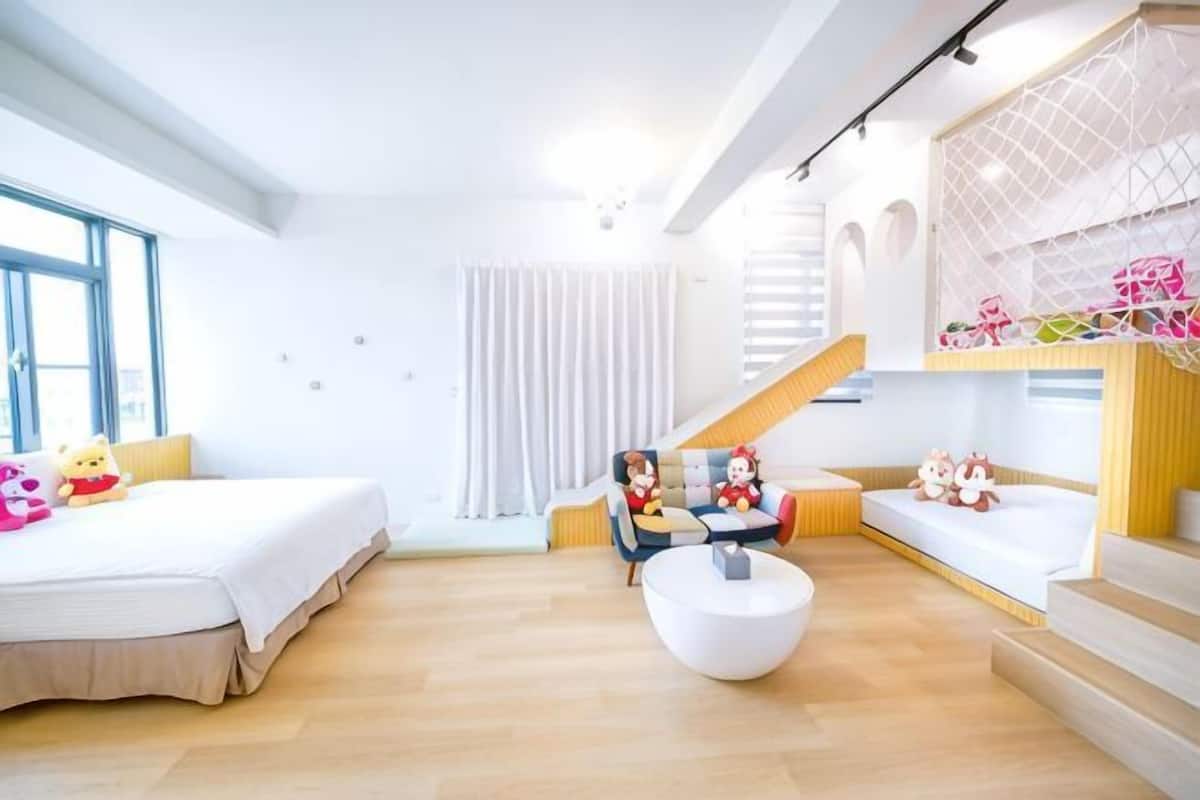 Ein modernes Hotelzimmer mit einem großen Bett, einer Sitzecke inklusive Sofa und Sesseln, einem runden weißen Tisch sowie einer Treppe mit Geländer.