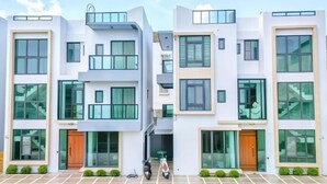 Un immeuble résidentiel moderne à plusieurs étages, doté de balcons, de grandes fenêtres et d’une allée carrossable dallée.