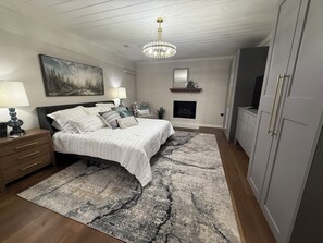 Ein Schlafzimmer mit Bett, Nachttischen, einem Chandelier, einem Kamin und einem Kleiderschrank.