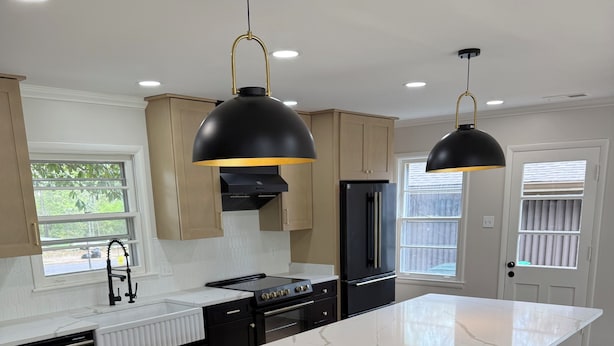 Una cucina moderna con una grande isola, mobili scuri e illuminazione a sospensione.