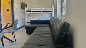 Une pièce avec un lit superposé, un canapé noir, une petite table et une chaise.