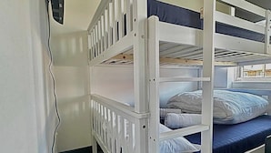 Une chambre avec un lit superposé, des barreaux blancs et une literie bleue.
