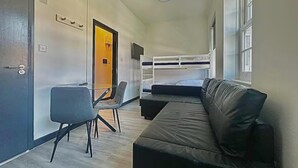Une pièce comprenant un lit superposé, un canapé, un bureau avec une chaise et une porte dotée d’une poignée.