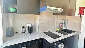 Une cuisine compacte équipée d’un lave-vaisselle intégré, d’une machine à café et d’un évier avec distributeur de savon.