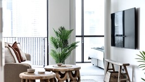 A modern living room with a sofa, two wooden side tables, a potted plant, a bench, and a TV mounted on the wall. - Ocean Views at Yves Mermaid Beach (Mermaid Beach)