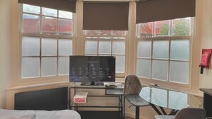 Habitación de esquina con cama, escritorio, silla y televisor.