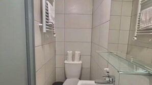 Un baño pequeño y moderno con inodoro, lavamanos y cabina de ducha de vidrio.