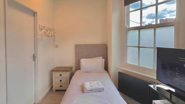 Un dormitorio ordenado con cama, mesita de noche y televisión.