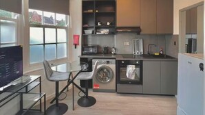 Un espacio habitable compacto con kitchenette, lavadora, comedor con mesa y sillas, y una cama.