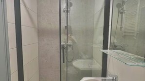 A glass-enclosed shower with a glass shelf and a sink. - Golders Green Cozy City Studio in London (London)