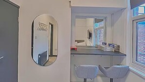 A modern bathroom with a large mirror, two bar stools, a countertop, and a window with a view of a brick building. - Golders Green Cozy City Studio in London (London)