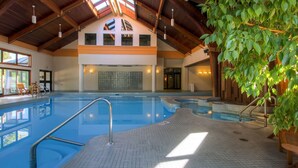 An indoor swimming pool with a tiled floor, a wooden ceiling, and a seating area with a plant. - Woods Village 43 (Killington)