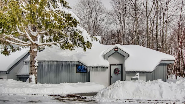 A snow-covered building with a door and a wreath, surrounded by trees and snow. - Woods Village 43 (Killington)