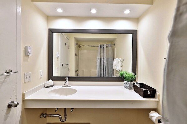 A bathroom with a white sink, mirror, and shower curtain. There are towels and a small plant on the counter. - Hotel Style Condo Promising a Comfortable and Convenient Retreat Right in the Heart of Vermont ski Country (Killington)