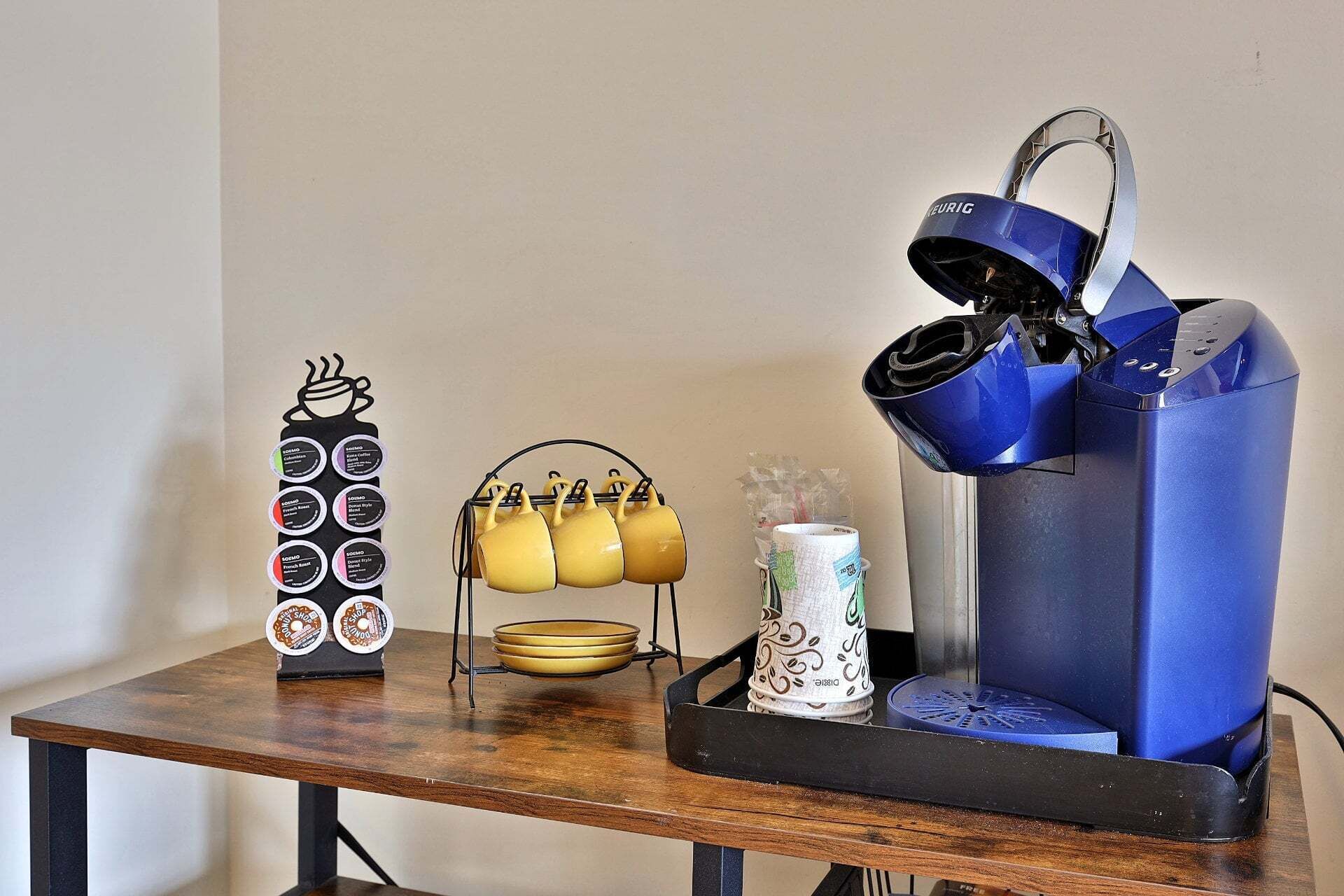 A coffee machine, a mug holder, and a coffee pod dispenser on a wooden table.