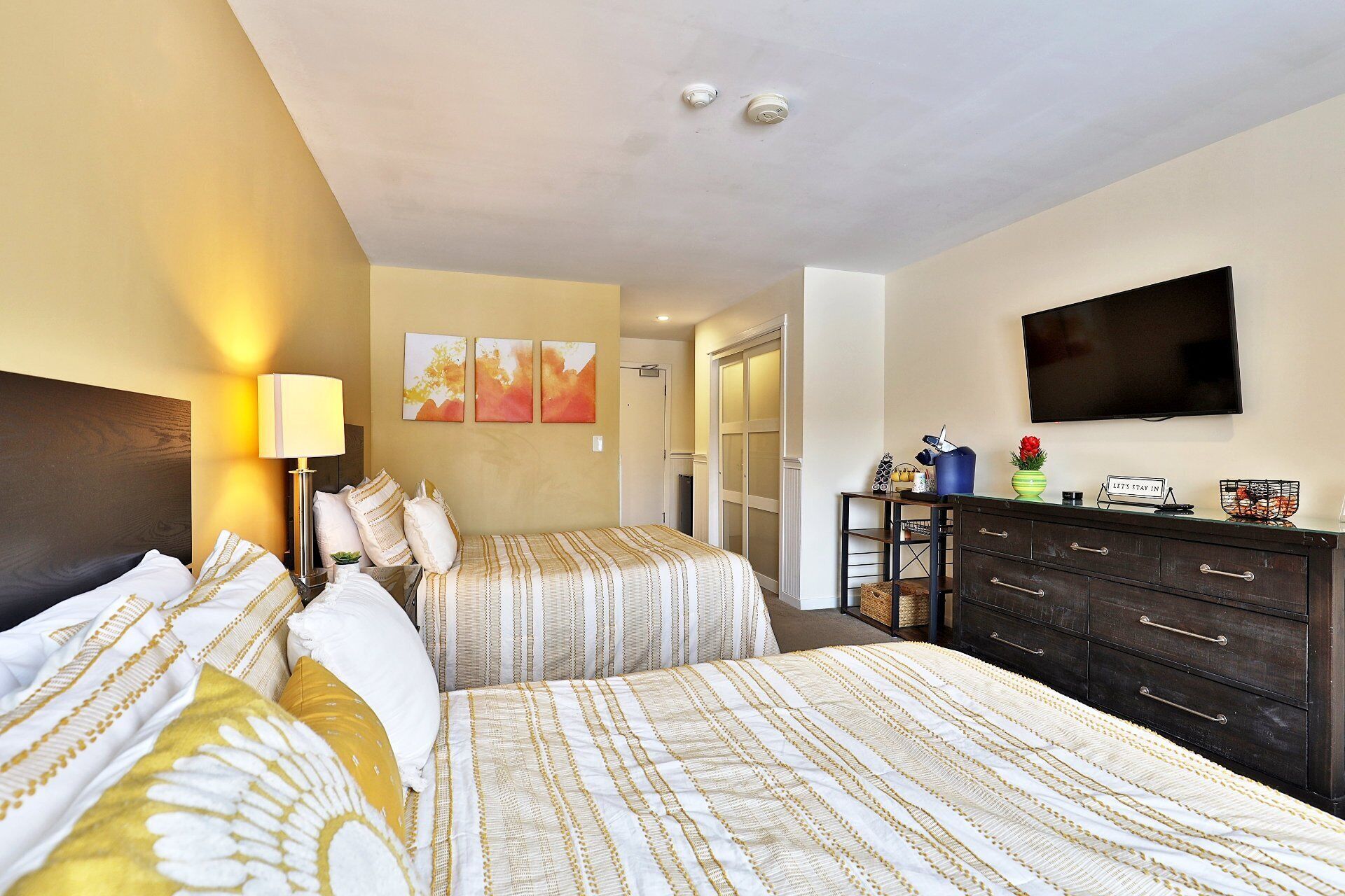 A hotel room with two beds, a TV, a dresser, and artwork on the wall.