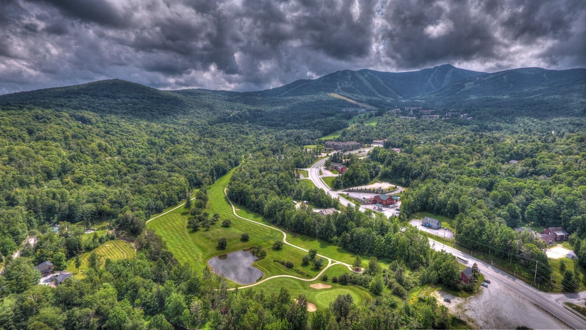 Vista aérea de um campo de golfe com um clube, rodeado por vegetação exuberante e montanhas.