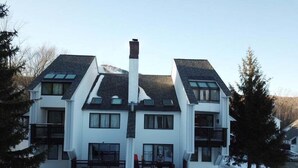 A multi-story residential building with a symmetrical design, featuring a central chimney, large windows, and a snow-covered ground. - Sunrise - W Glade J-1 (Killington)