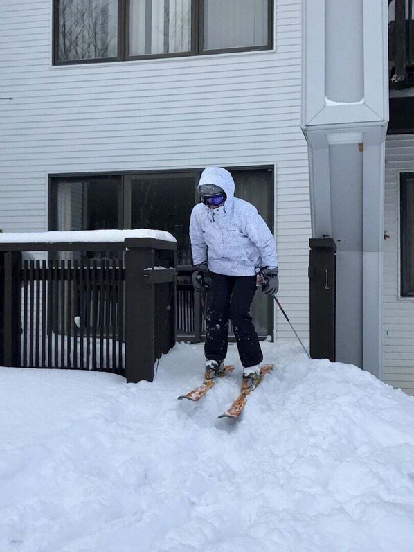 Una persona esquiando en un sendero cubierto de nieve, frente a un edificio con una reja negra y una puerta.