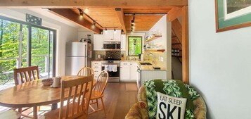 Una cocina moderna con armarios blancos, horno integrado y comedor con mesa y sillas de madera.