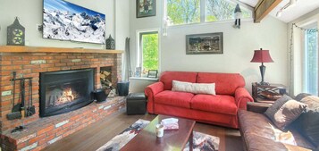 Un salón acogedor con chimenea, sofá rojo y un ventanal grande.