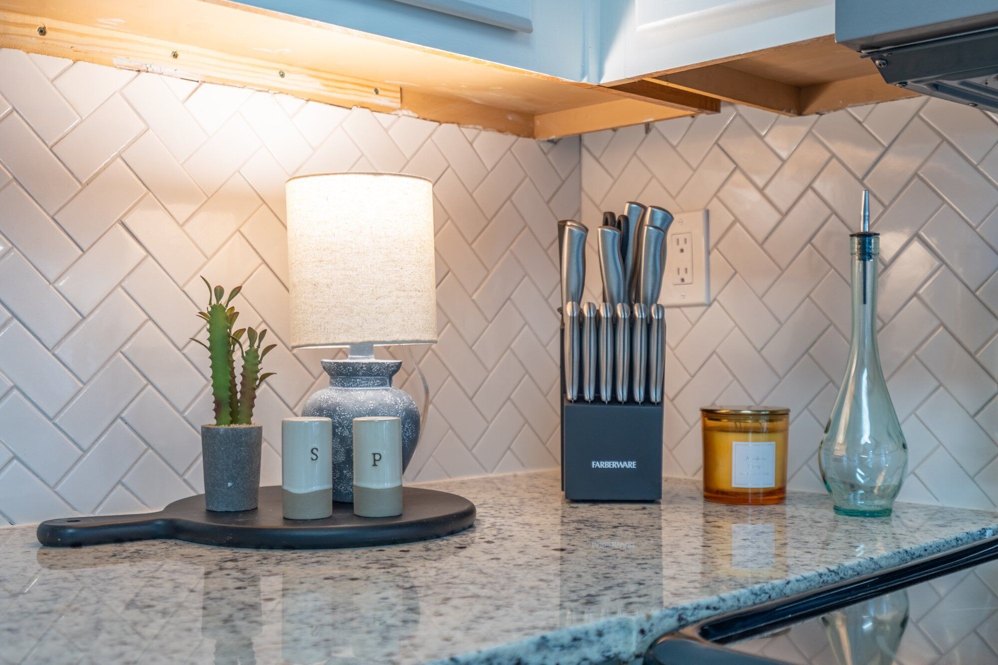 A kitchen counter with a knife block, a lamp, salt and pepper shakers, a candle, and a glass bottle.