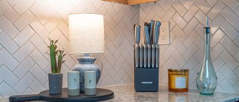 A kitchen counter with a knife block, a lamp, salt and pepper shakers, a candle, and a glass bottle.